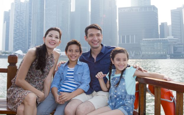 Joyful family capturing memories on a cruise in Singapore, posing against the scenic river backdrop, creating cherished moments together.